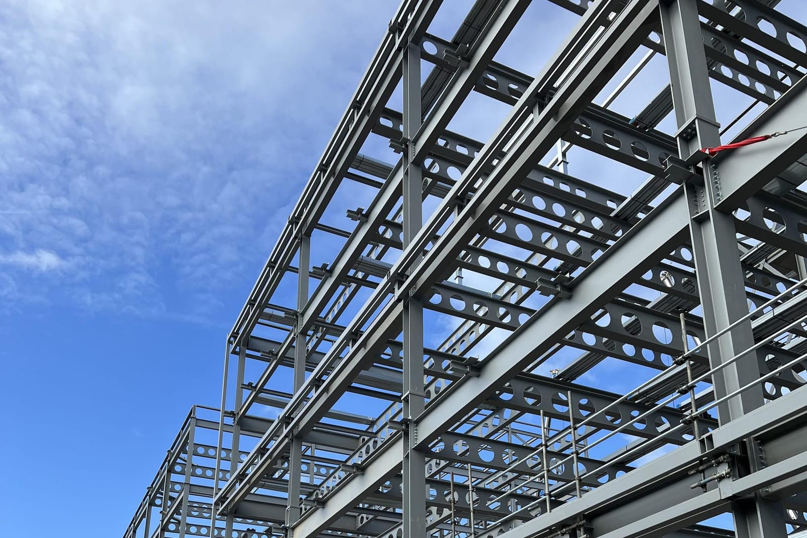 Steel frame under erection, cellular beams and columns against a blue sky.